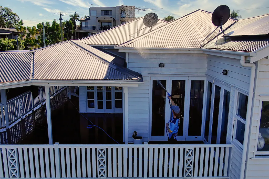 kg-gutter-cleaning-2 Kleen Genie technician spraying and rinsing a roof gutter on Australian style house