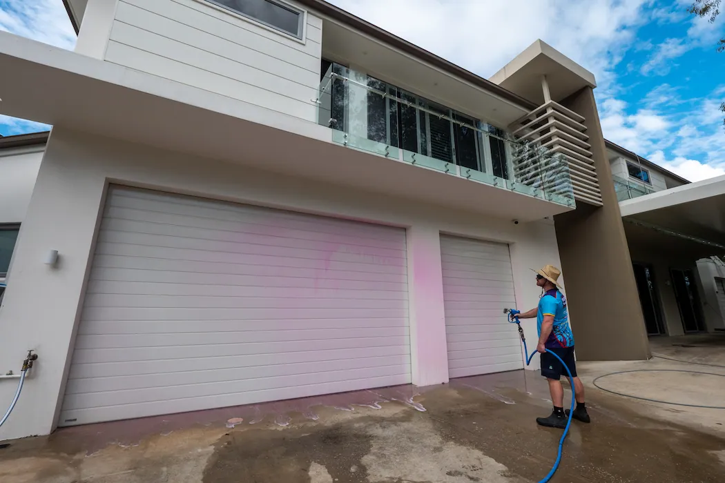 Kleen Genie technician spraying chemicals on external garage doors while house washing