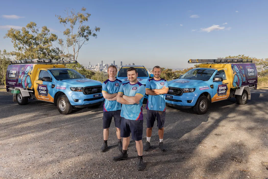 Three Kleen Genie technicians standing in front of branded work vehicles with Brisbane city on the horizon